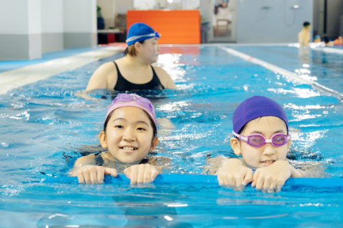 写真②　ビート板で泳ぐ子ども
キャプ　プールでは子どもたちの歓声が響く