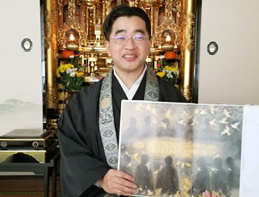 （画像アイキャッチ兼用：絵本を掲げる福間住職）