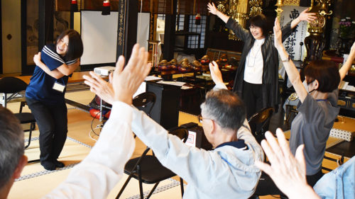 （画像：アトラクションで認知機能低下を防ぐ体操を行う参加者）