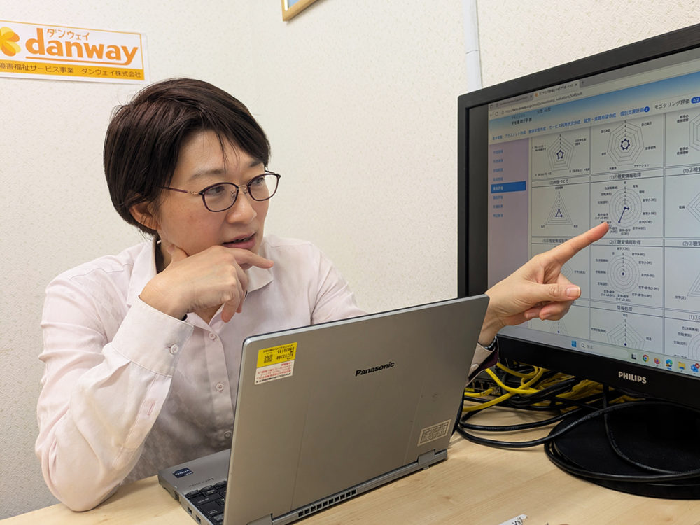 （画像１アイキャッチ兼用：「シームレスバディ」の画面を見せて説明するダンウェイの高橋社長。レーダーチャートで障害のある人の能力が分かる）