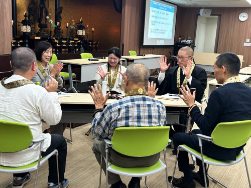 （画像アイキャッチ兼用：模擬カフェで、場をほぐす遊びを教える浄福寺の髙橋さん（左奥）。右奥は小川住職＝京都市東山区の源光院）