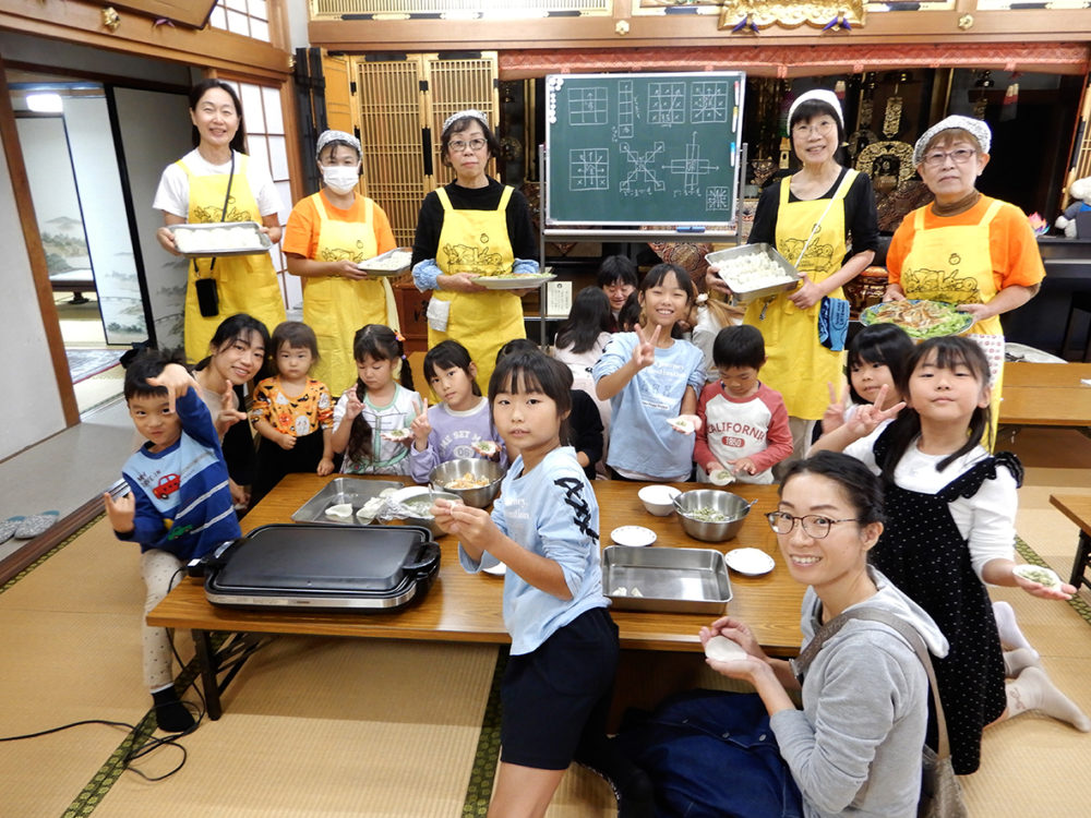 （画像3アイキャッチ兼用：食事の手作りギョーザを包む子どもたちとスタッフら）