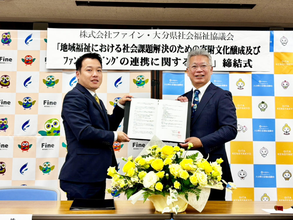 （画像アイキャッチ兼用：協定書を交わす大分県社会福祉協議会の佐藤会長（右）とファインの茶屋元取締役統括本部長（大分県社協提供））